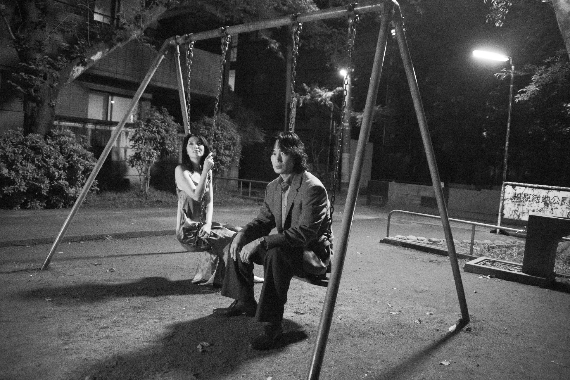 夜の公園でブランコに乗る男女