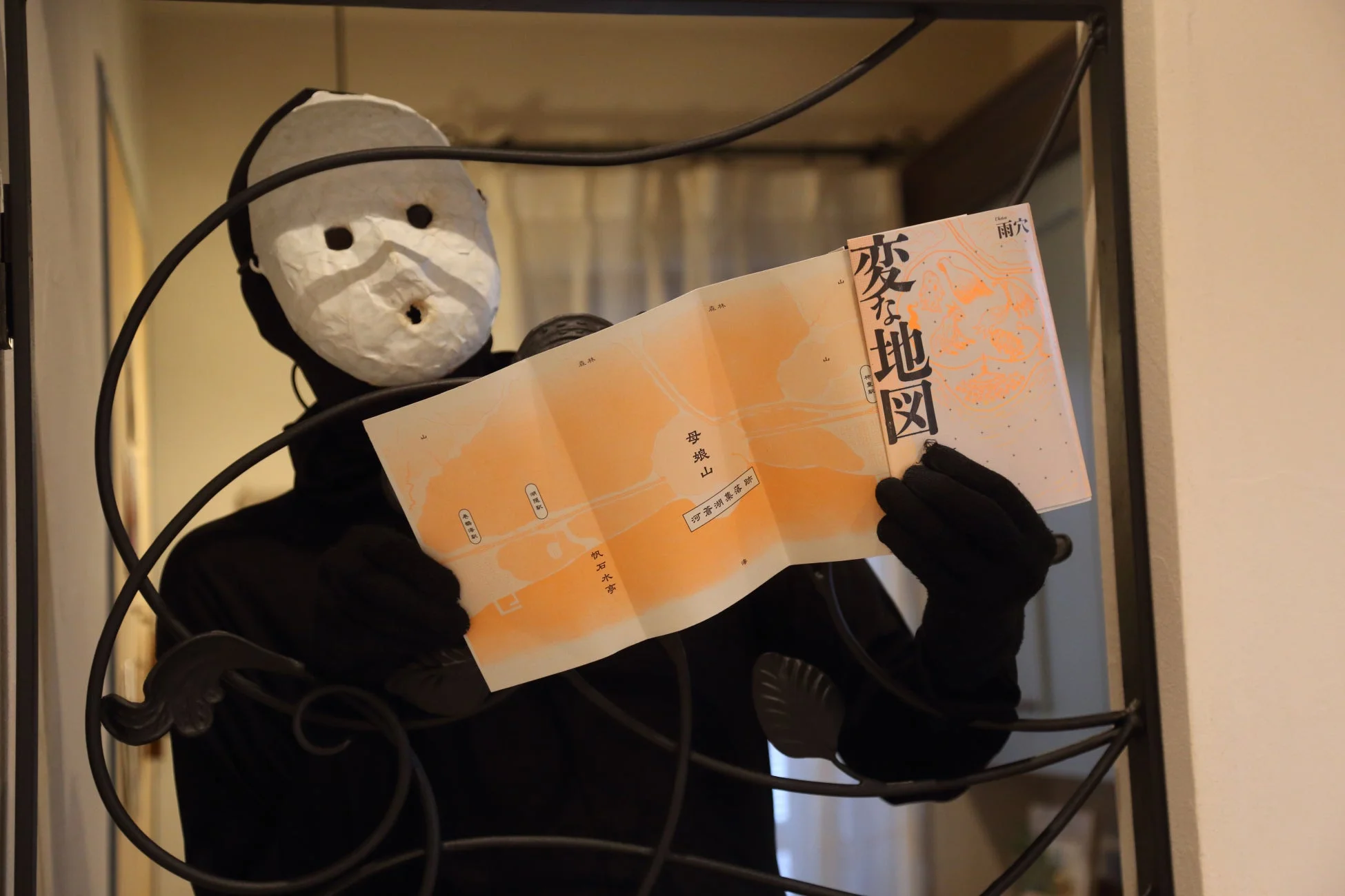 白い不気味なマスクを被った人物が「変な地図」と題された地図を広げている